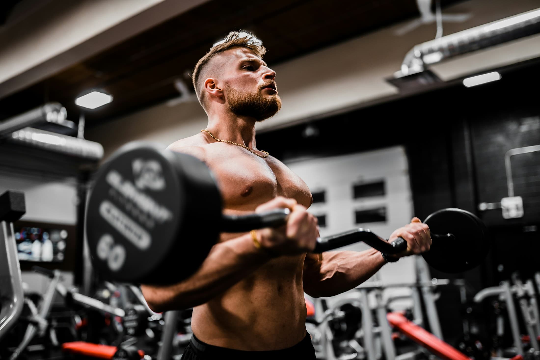 Shirtless athlete mid-rep on a curl bar in a dimly lit gym